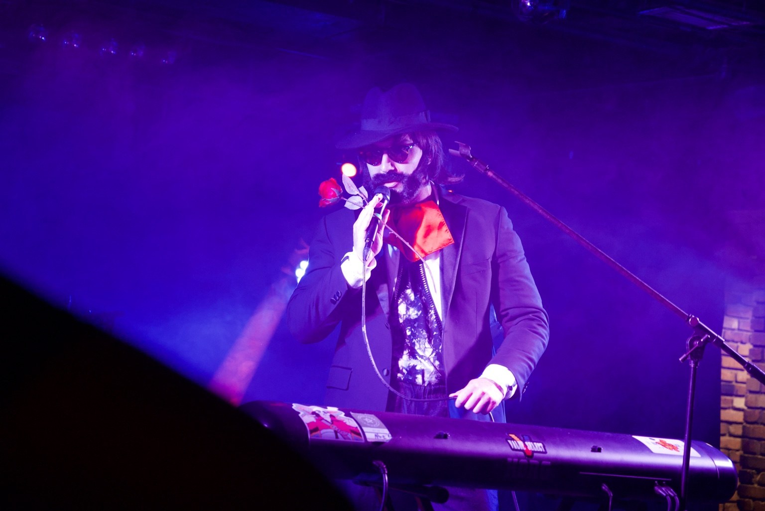Performer singing and playing keyboard under purple lights